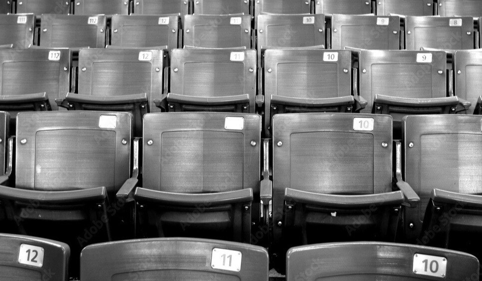 Black and white photo of empty, numbered stadium seats arranged in rows. The wooden seats, marked with numbers like 10, 11, and 12, evoke nostalgia akin to flipping through an innovative mobile application that preserves history with a modern twist.