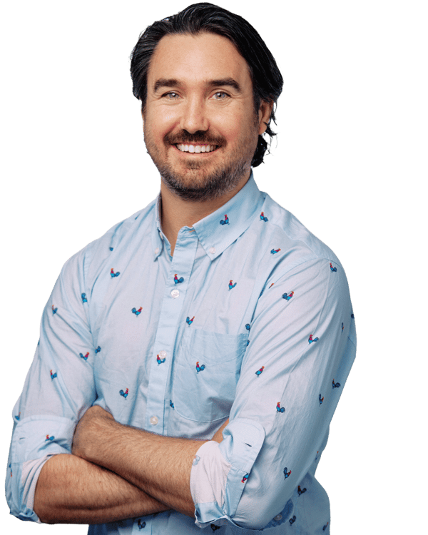 A smiling man with medium-length dark hair and a beard, wearing a light blue button-up shirt with small, colorful rooster patterns, stands with his arms crossed against a plain background—an everyday look for professionals in software companies in Minneapolis.